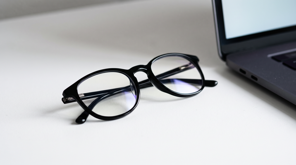 Lens with blue-light filter showing a faint blue-violet reflection next to a laptop